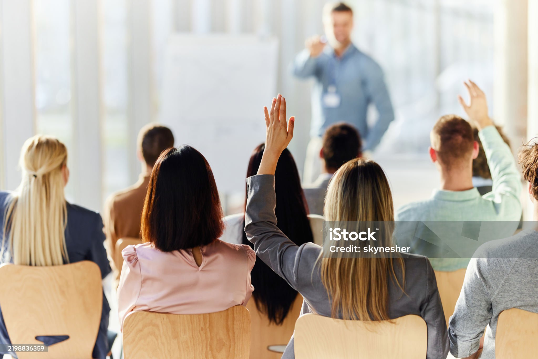 Rear view of a businesswoman raising her hand to ask a question on an education event in board room.